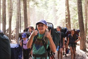 A summer camp camper gives two thumbs up on a backpacking trip