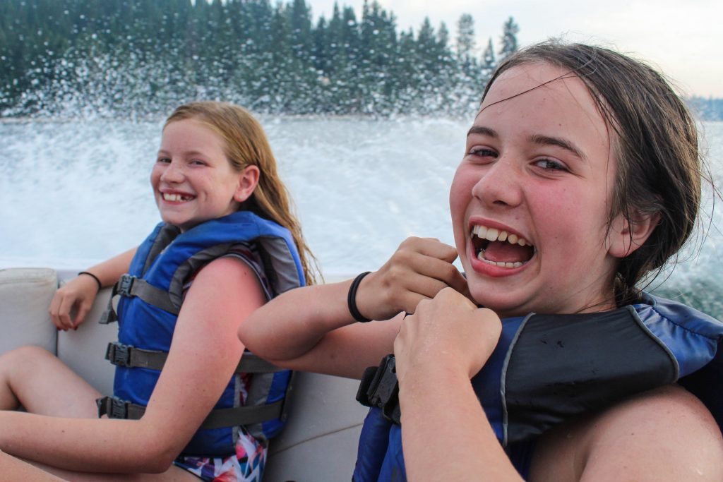 Two campers in life jackets smile on a ski boat at an American summer camp