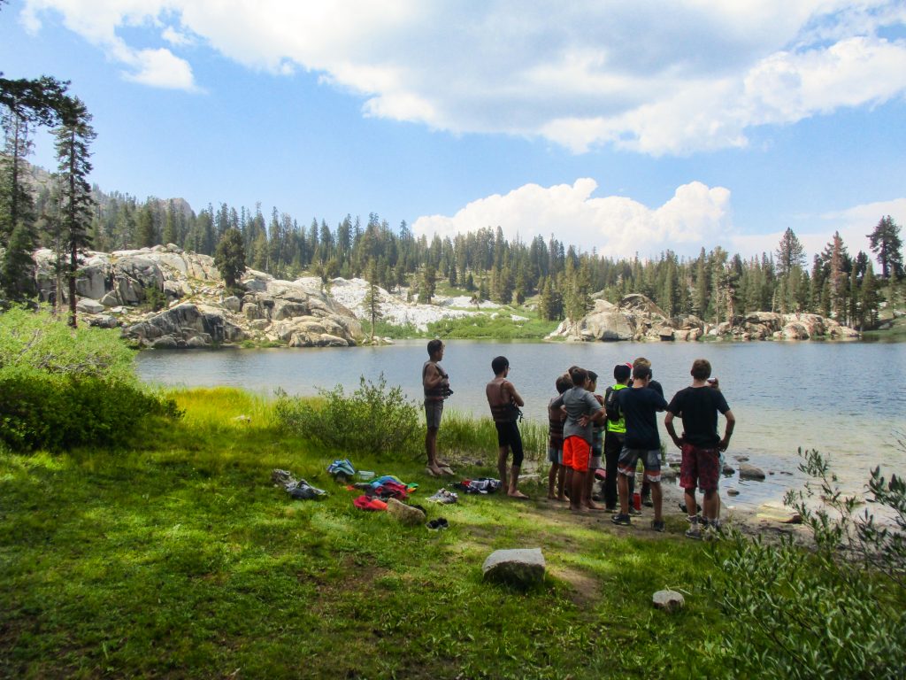 A group of backpackers looks at a mountain lake in the high sierra