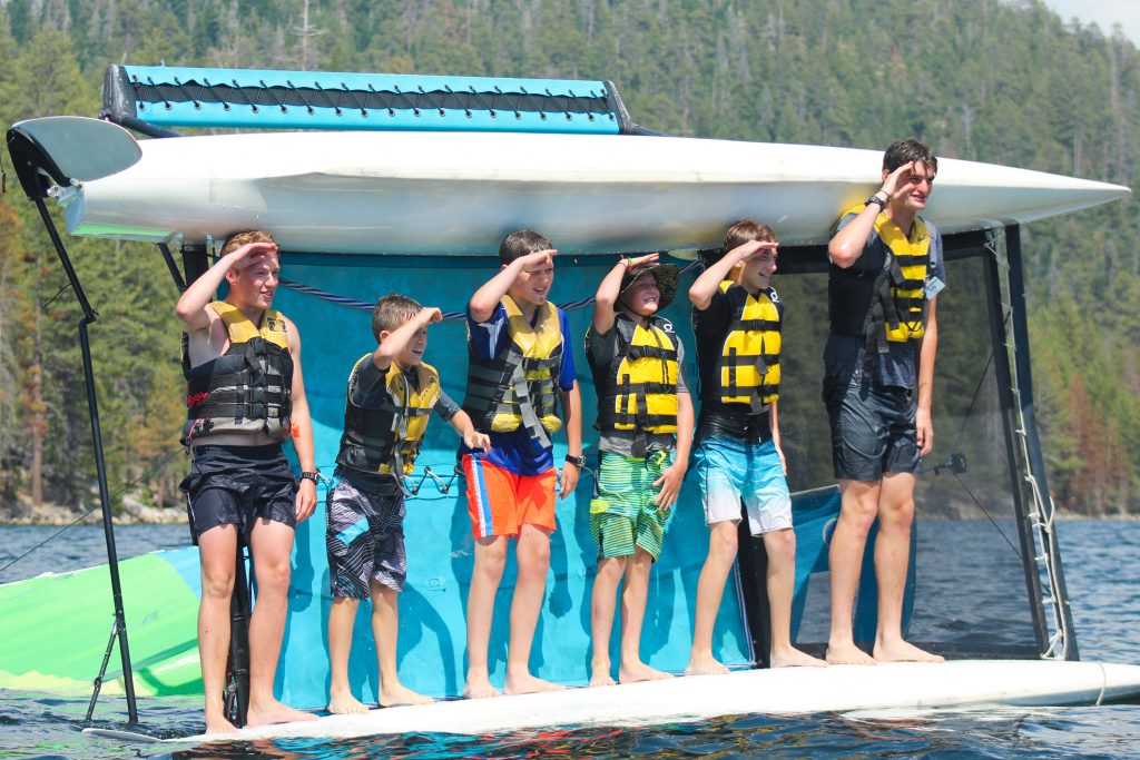 A cabin of summer camp boys and their counselor stand a salute on a capsized Hobie catamaran at Gold Arrow Camp