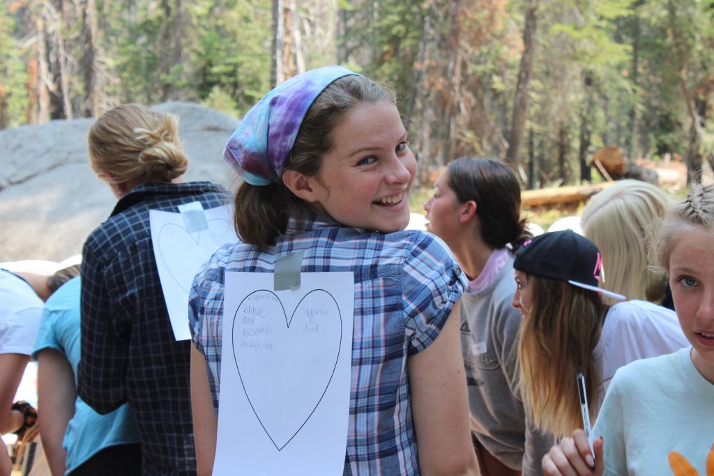 A girl at a summer camp in California smiles at the camera with a heart taped to her back