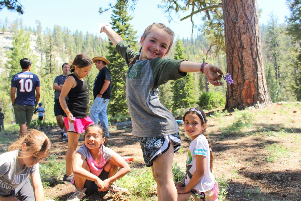 A young smiling female camper poses on a mountain top at summer camp in California.